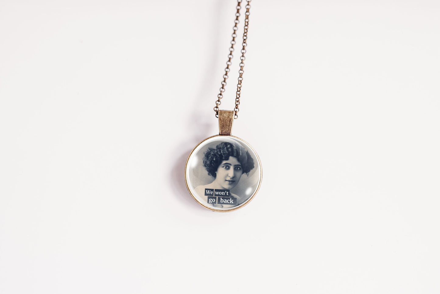 Product photo of a 1-inch glass cabochon pendant necklace featuring “We Won’t Go Back” with a black-and-white portrait of a curly-haired vintage woman on a 20-inch chain.