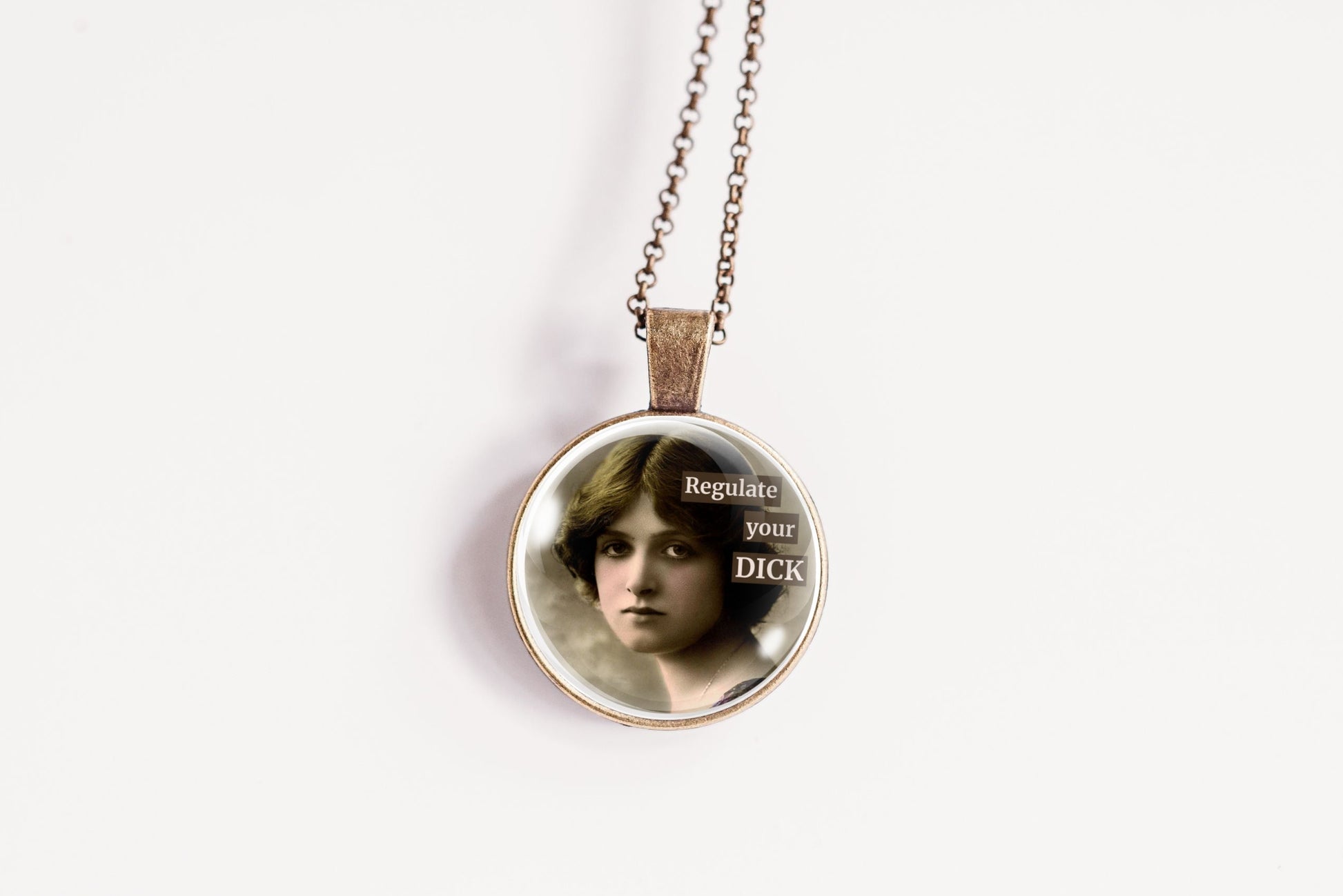 Product photo of a 1-inch glass cabochon pendant necklace featuring “Regulate Your Dick” with a sepia portrait of a vintage-style woman on a 20-inch chain.