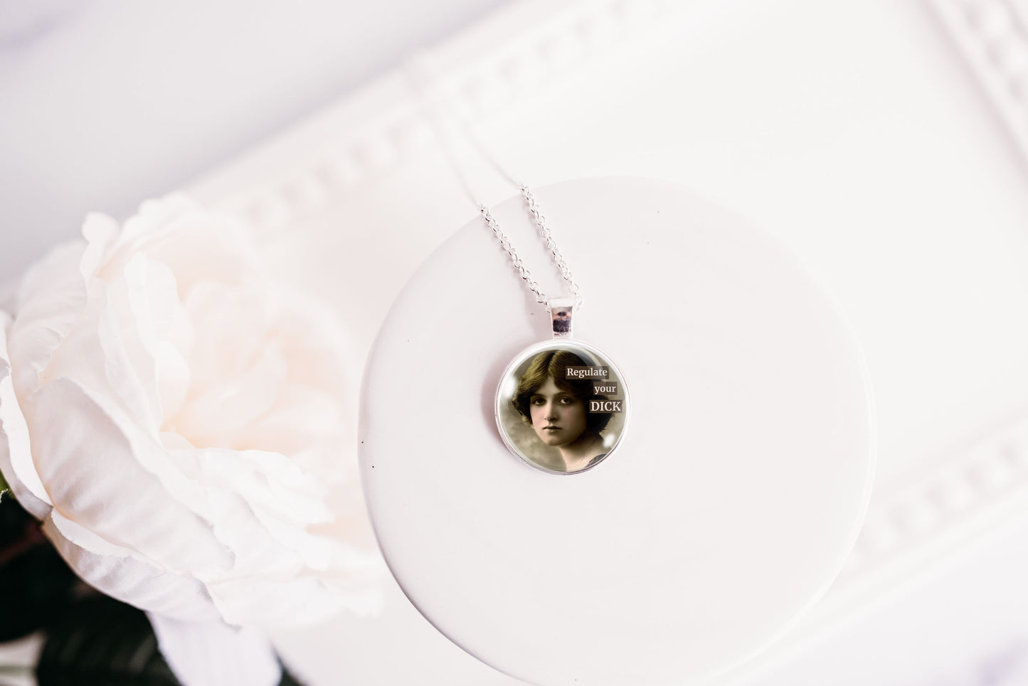 Product photo of a 1-inch glass cabochon pendant necklace featuring “Regulate Your Dick” with a sepia portrait of a vintage-style woman on a 20-inch chain.