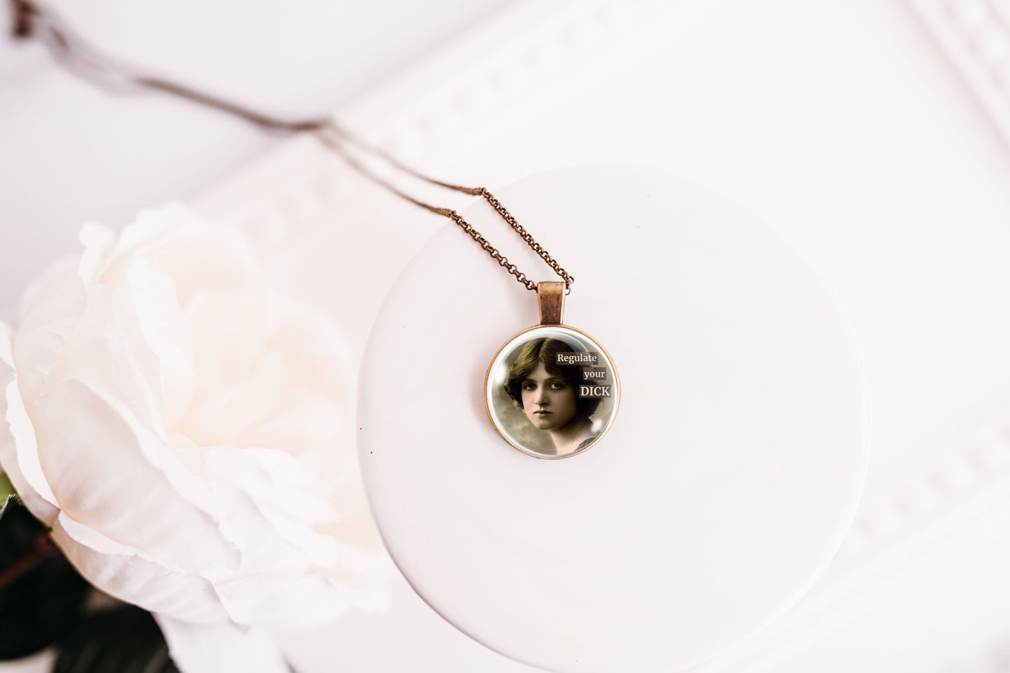 Product photo of a 1-inch glass cabochon pendant necklace featuring “Regulate Your Dick” with a sepia portrait of a vintage-style woman on a 20-inch chain.
