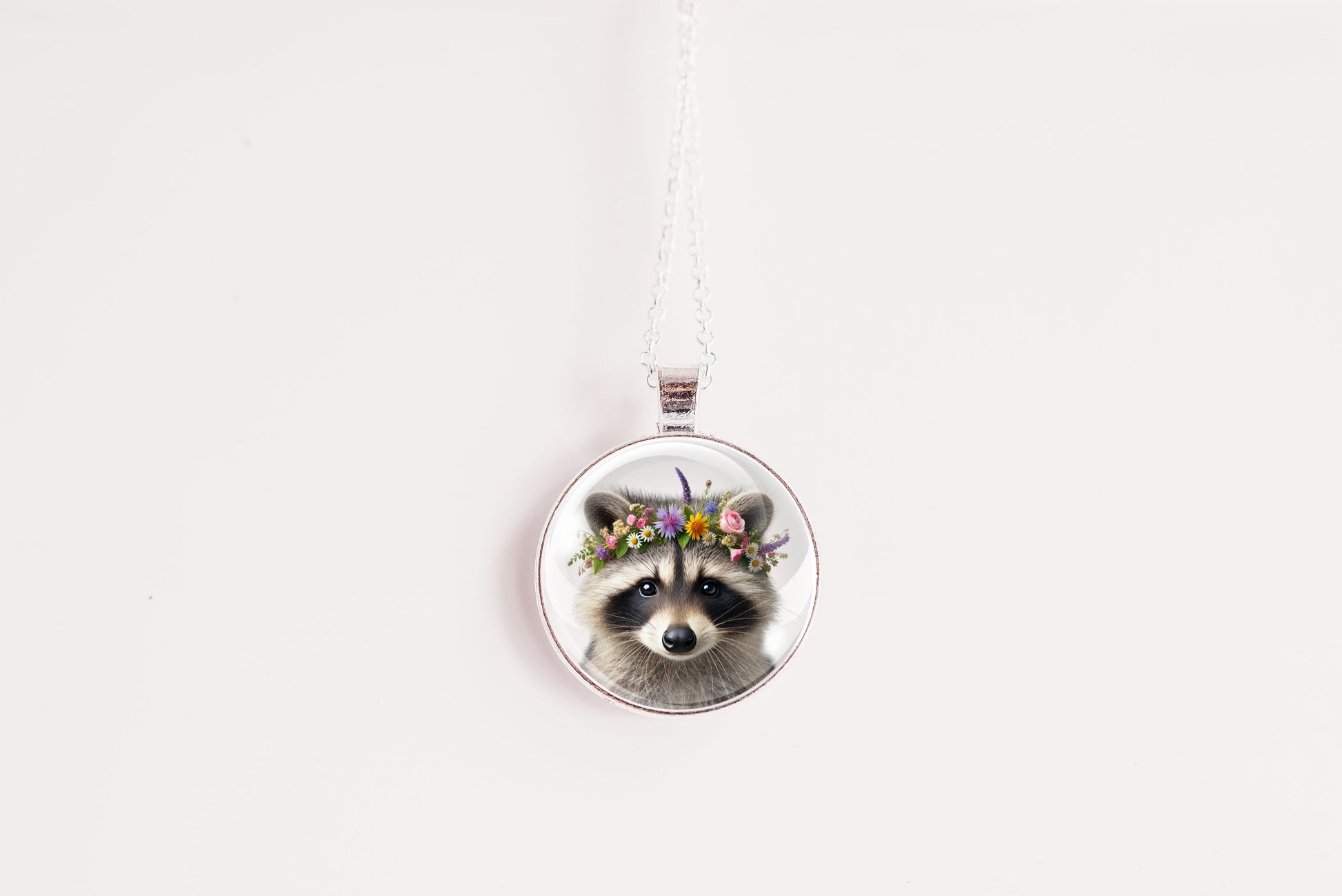 Close up image of a raccoon wearing a whimsical flower crown set in a silver-toned bezel. 
