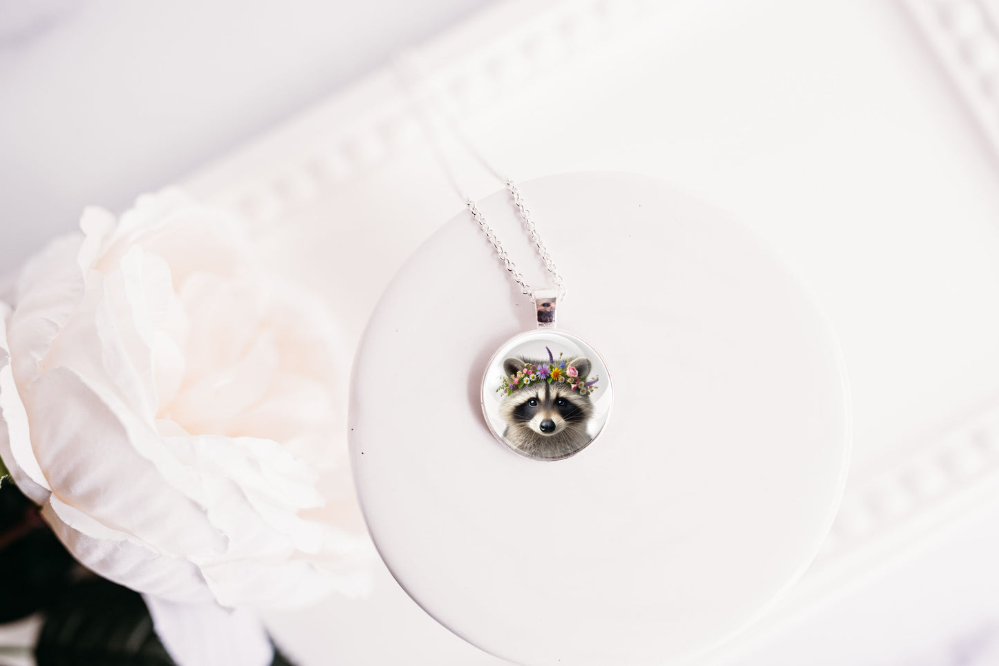 Close up image of a raccoon wearing a whimsical flower crown set in a silver-toned bezel. 