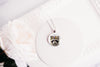 Close up image of a raccoon wearing a whimsical flower crown set in a silver-toned bezel. 