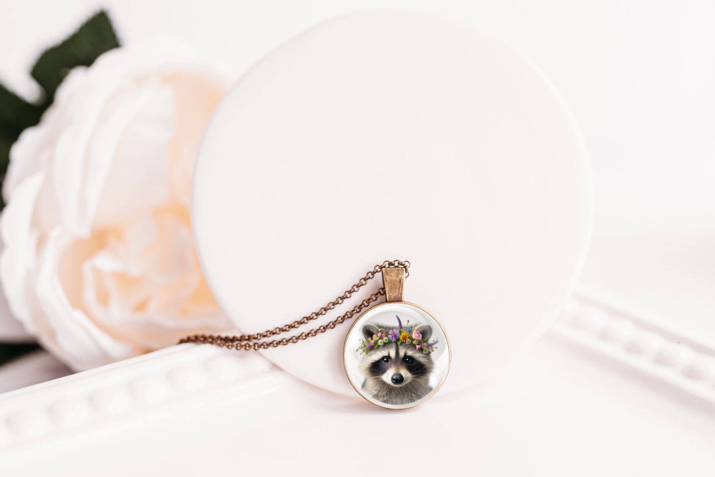 Close up image of a raccoon wearing a whimsical flower crown set in a bronze-plated bezel. 