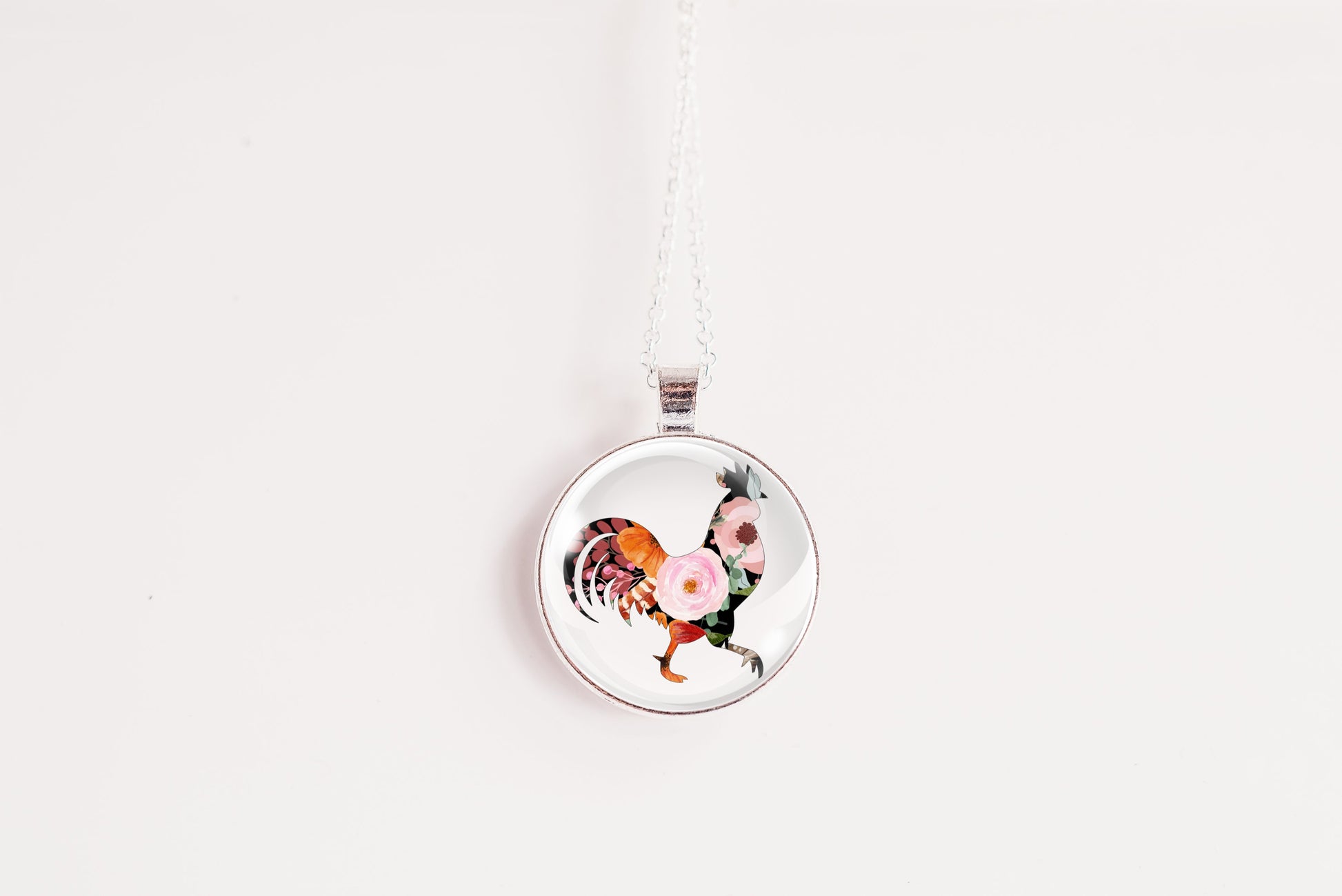 Round pendant with a design of a floral silhouette rooster on a white background