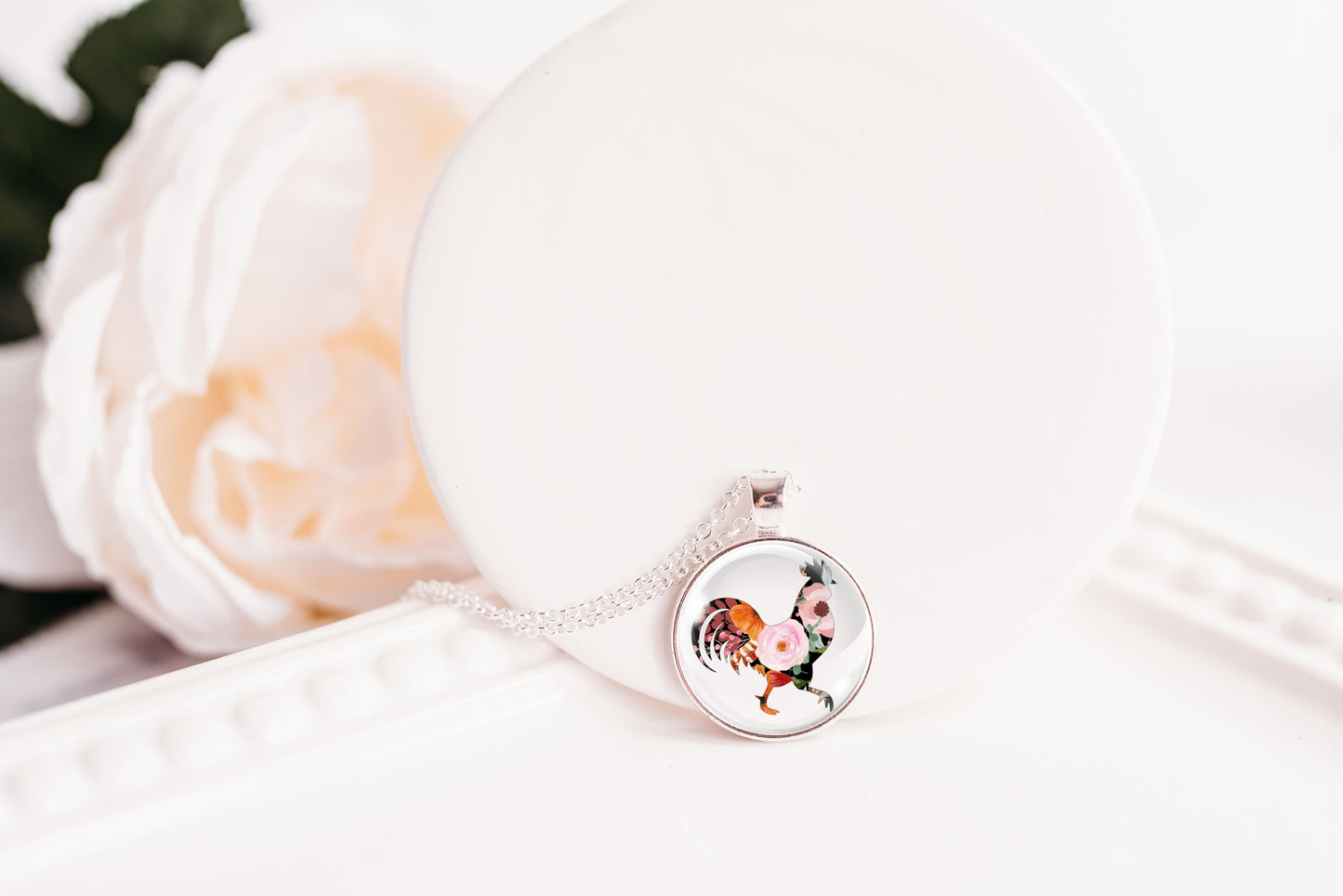 Necklace with a pendant featuring rooster design on a white surface with flowers.