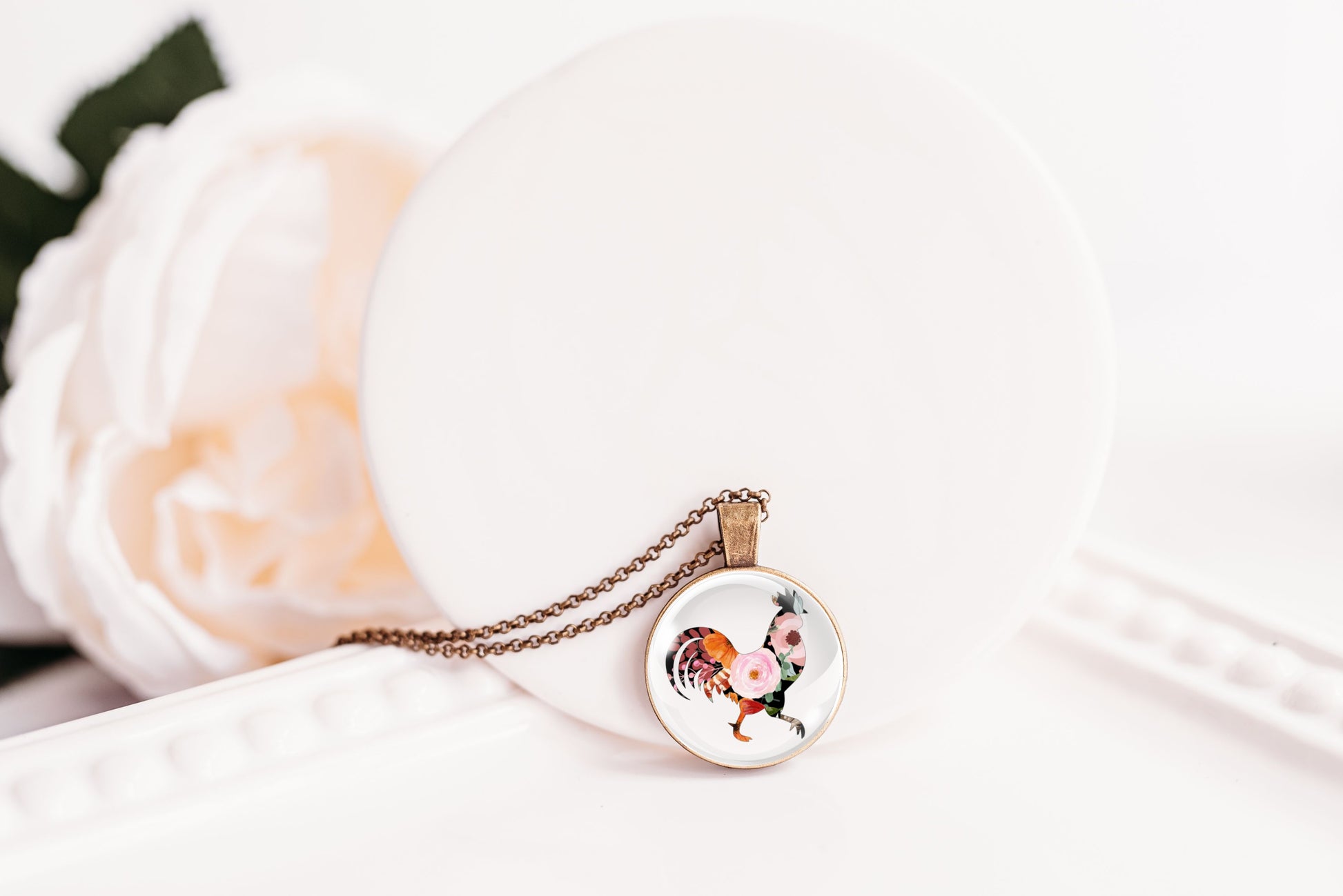 Necklace with a round pendant featuring a rooster design on a white surface.