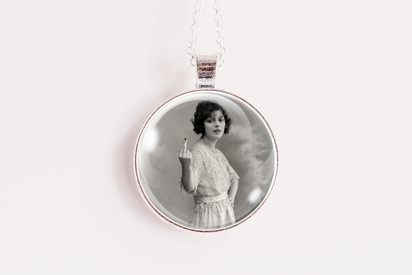 A silver round pendant necklace featuring a black and white vintage portrait of a woman, suspended from a thin silver chain against a plain white background.
