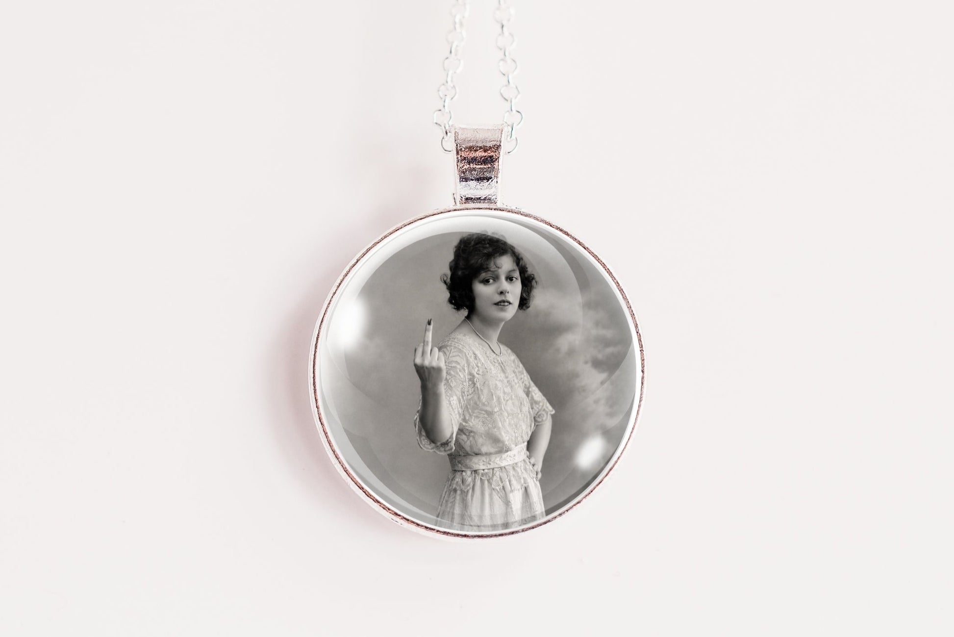 A silver round pendant necklace featuring a black and white vintage portrait of a woman, suspended from a thin silver chain against a plain white background.