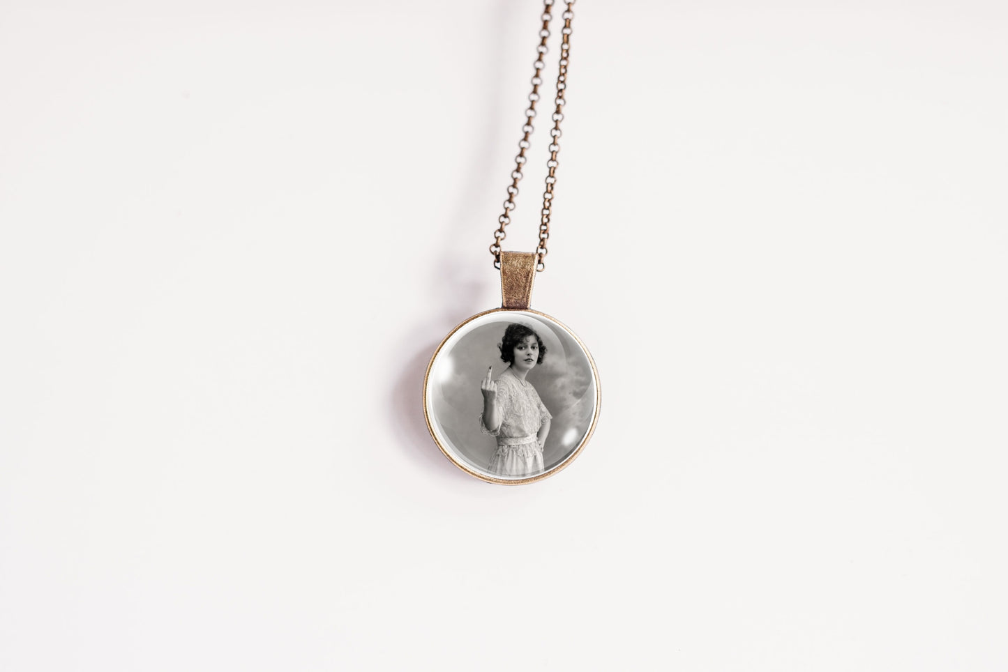 A vintage-style pendant necklace featuring a circular glass cabochon with a black-and-white portrait of a woman, suspended from a delicate bronze-toned chain against a plain white background.