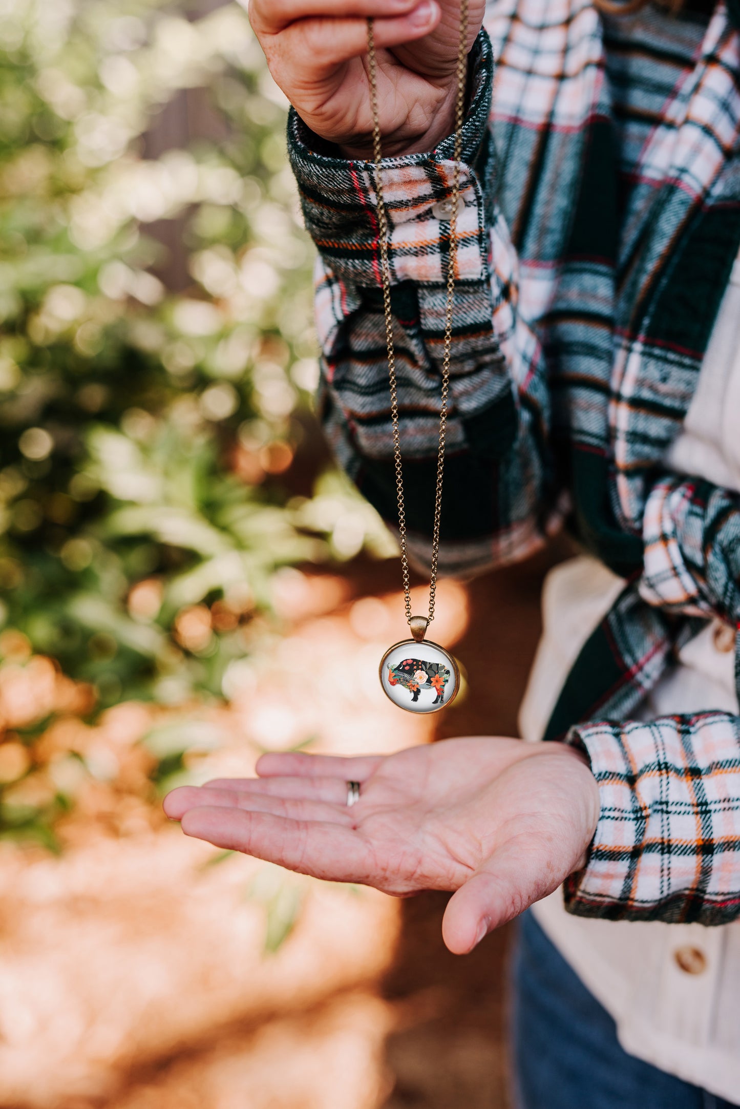Floral silhouette bison pendant necklace held by a woman wearing a green plaid flannel shirt
